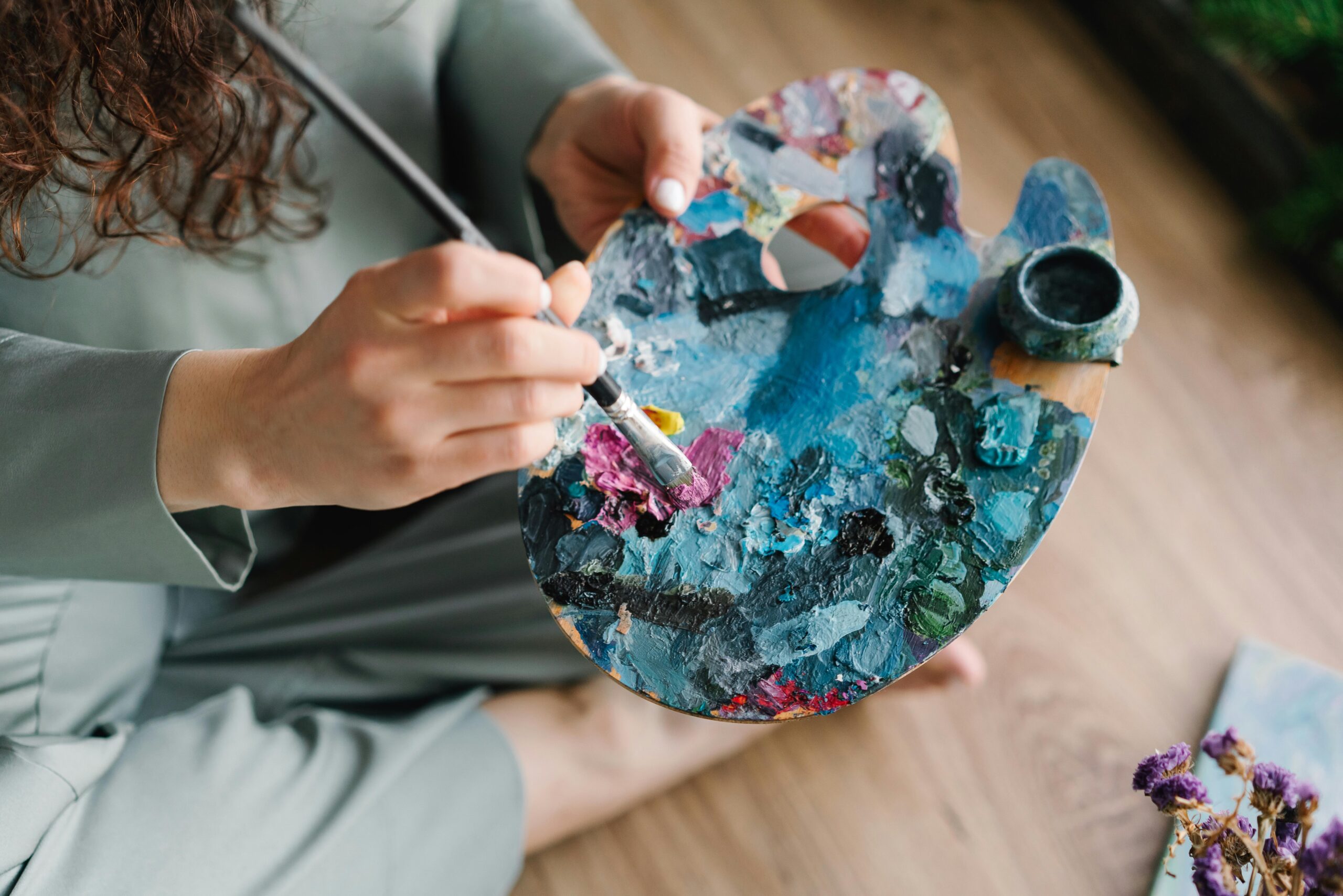 Close-up of hands painting on a colorful palette, showcasing creativity and artistry.